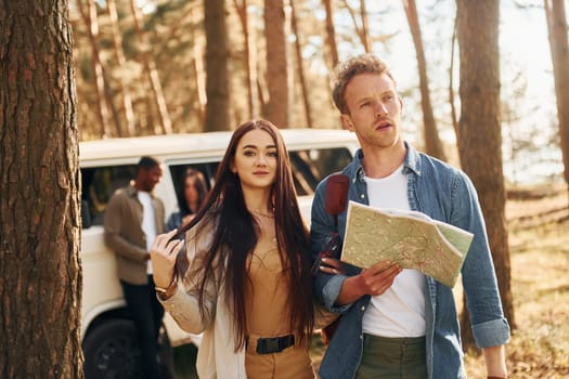 Standing near the car. Group of young people is traveling together in the forest at daytime.