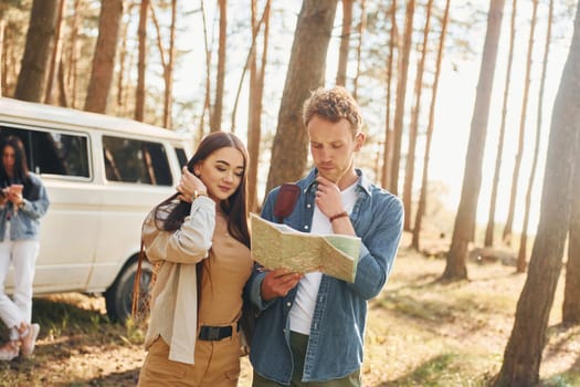 Looking for location by using map. Group of young people is traveling together in the forest at daytime.