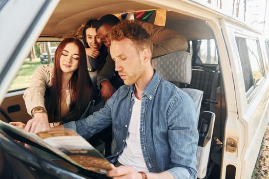 Sitting in the car. Group of young people is traveling together in the forest at daytime.