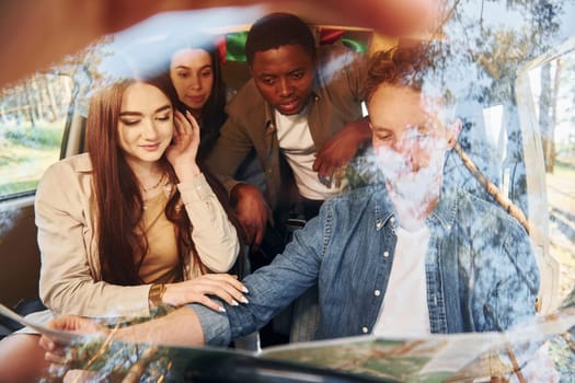 Sitting in the car. Group of young people is traveling together in the forest at daytime.