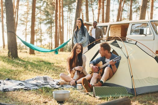 Camp and car. Group of young people is traveling together in the forest at daytime.