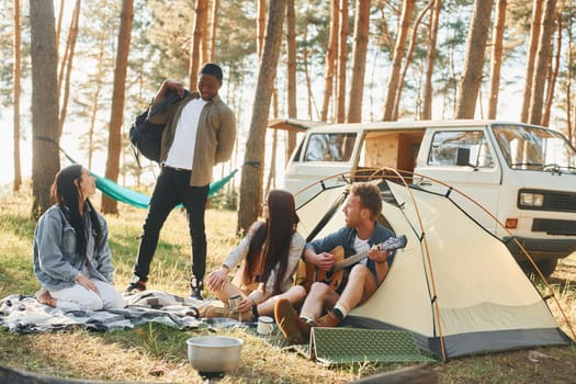 Camp and car. Group of young people is traveling together in the forest at daytime.