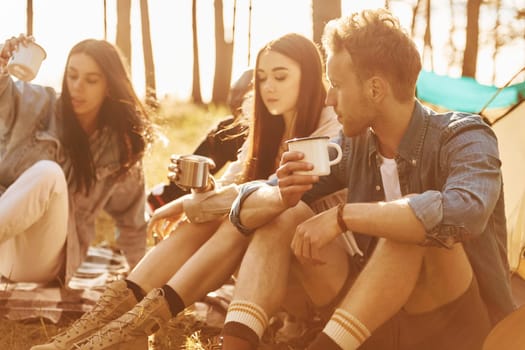 Sitting and resting. Group of young people is traveling together in the forest at daytime.