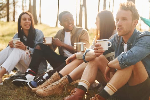 Sitting and resting. Group of young people is traveling together in the forest at daytime.