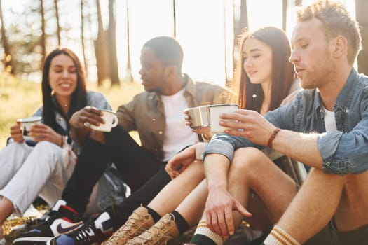 Sitting and resting. Group of young people is traveling together in the forest at daytime.