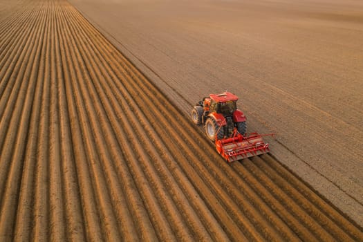PRAGUE , CZECH REPUBLIC - MARCH 18 2022: Tractor drives preparing beds for planting seedlings in cultivated soil. Heavy machine tills on field helping with agriculture aerial view