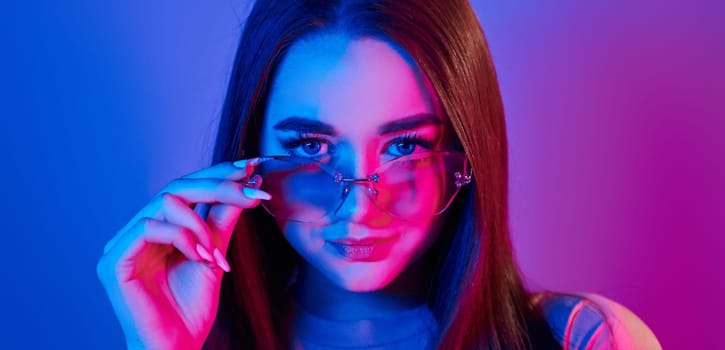 Neutral facial expression. Fashionable young woman standing in the studio with neon light.