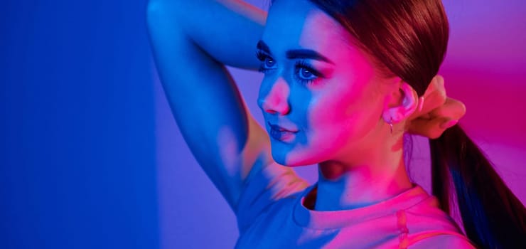 Side view. Fashionable young woman standing in the studio with neon light.