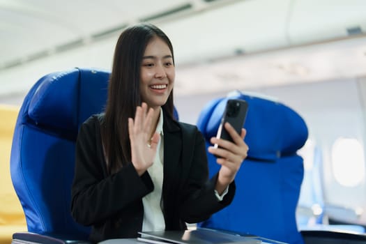 Asian business woman passenger sitting on business class luxury plane while working using smart phone mobile talking or video conference and travel concept.