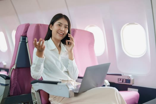 Asian business woman passenger sitting on business class luxury plane while working using smart phone mobile talking or video conference and travel concept.