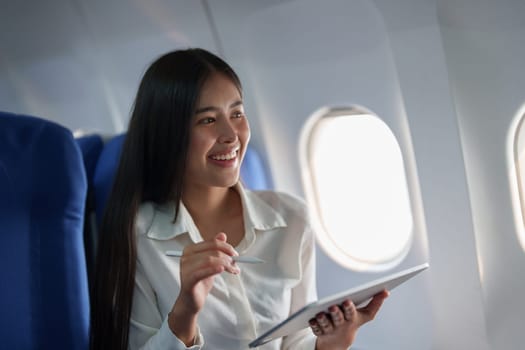 Asian attractive business woman passenger sitting on business class luxury plane while tablet computer while travel concept.