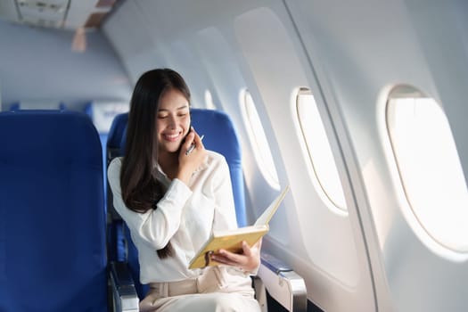 Asian business woman passenger sitting on business class luxury plane while working using smart phone mobile talking and use notebook while travel concept.