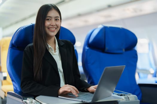 Asian business woman passenger sitting on business class plane while working on laptop computer with simulated space using on board wireless connection.