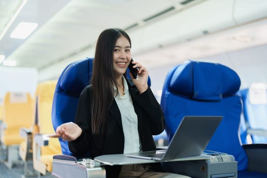 Asian business woman passenger sitting on business class luxury plane while working using smart phone mobile talking and use laptop computer with simulated space using on board wireless connection