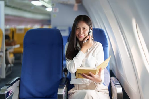 Asian business woman passenger sitting on business class luxury plane while working using smart phone mobile talking and use notebook while travel concept.