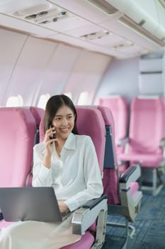 Asian business woman passenger sitting on business class luxury plane while working using smart phone mobile talking or video conference and travel concept.