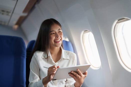 Asian attractive business woman passenger sitting on business class luxury plane while tablet computer while travel concept.