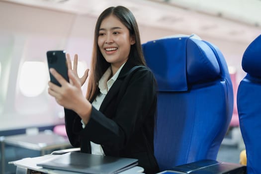 Asian business woman passenger sitting on business class luxury plane while working using smart phone mobile talking or video conference and travel concept.