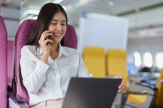 Asian business woman passenger sitting on business class luxury plane while working using smart phone mobile talking or video conference and travel concept.