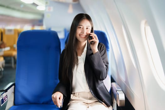 Asian business woman passenger sitting on business class luxury plane while working using smart phone mobile talking or video conference and travel concept.