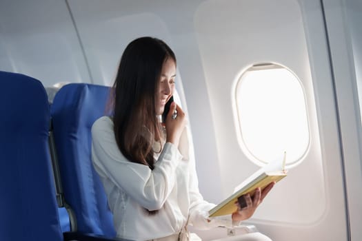 Asian business woman passenger sitting on business class luxury plane while working using smart phone mobile talking and use notebook while travel concept.