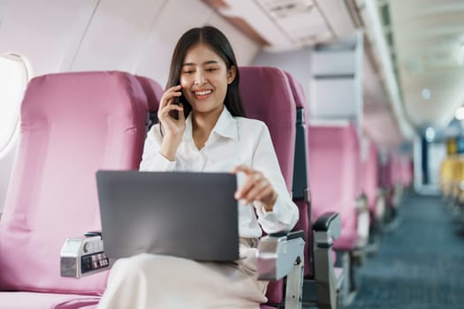 Asian business woman passenger sitting on business class luxury plane while working using smart phone mobile talking or video conference and travel concept.