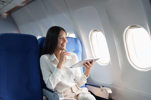 Asian attractive business woman passenger sitting on business class luxury plane while tablet computer while travel concept.