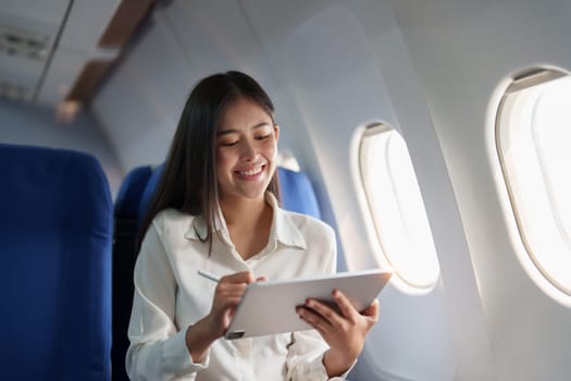 Asian attractive business woman passenger sitting on business class luxury plane while tablet computer while travel concept.