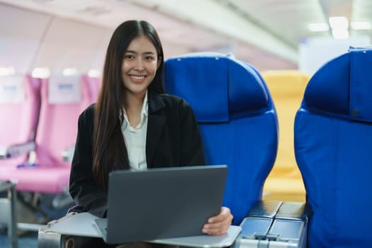 Asian business woman passenger sitting on business class plane while working on laptop computer with simulated space using on board wireless connection.
