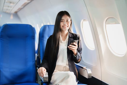 Asian business woman passenger sitting on business class luxury plane while working using smart phone mobile talking or video conference and travel concept.