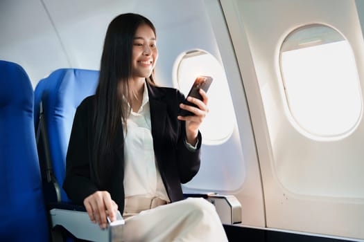 Asian business woman passenger sitting on business class luxury plane while working using smart phone mobile talking or video conference and travel concept.