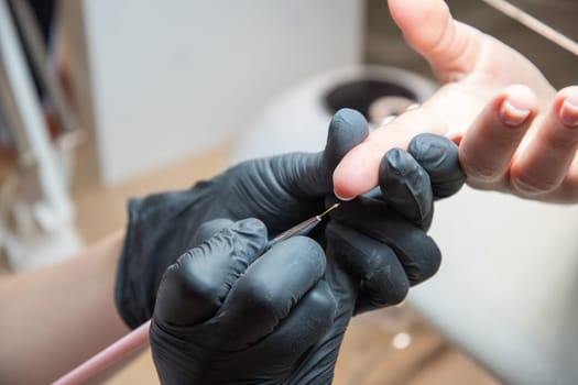 a master does a manicure to a client in a beauty salon and covers her nails with pink varnish, the master levels the edge of the varnish with a thin brush, High quality photo