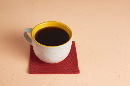 A white and yellow cup with black coffee on a light pink background.
