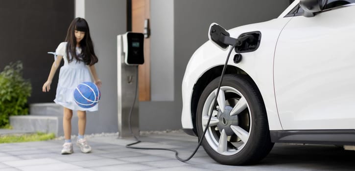 A playful and happy girl playing around at her home charging station providing a sustainable power source for electric vehicles. Alternative energy for progressive lifestyle.