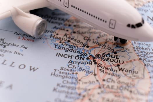 Miniature passenger plane on a colorful map focusing on Seoul, Inch'on South Korea through selective focus, background blur
