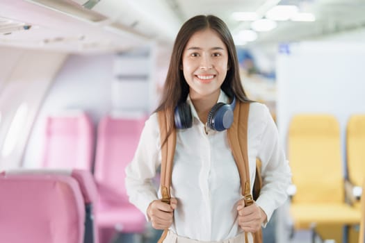 Young asian attractive woman travel by airplane, Passenger wearing headphone putting hand baggage in lockers above seats of plane.