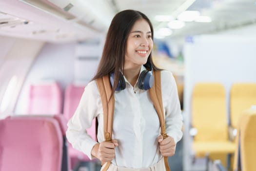 Young asian attractive woman travel by airplane, Passenger wearing headphone putting hand baggage in lockers above seats of plane.