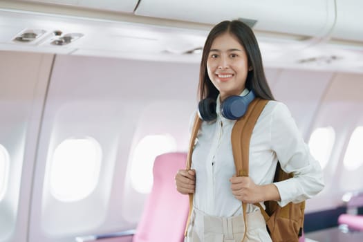 Young asian attractive woman travel by airplane, Passenger wearing headphone putting hand baggage in lockers above seats of plane.