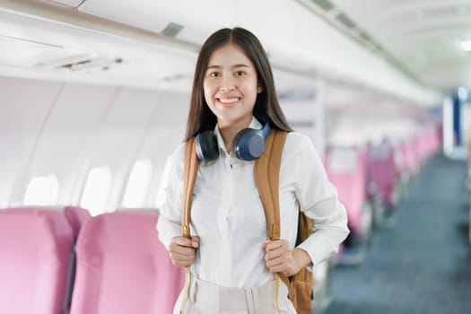 Young asian attractive woman travel by airplane, Passenger wearing headphone putting hand baggage in lockers above seats of plane.