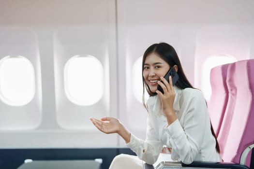 Asian business woman passenger sitting on business class luxury plane while working using smart phone mobile talking or video conference and travel concept.