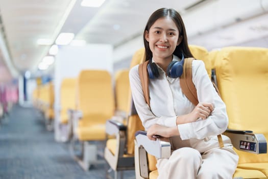 Young asian attractive woman travel by airplane, Passenger wearing headphone putting hand baggage in lockers above seats of plane.