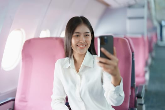 Asian business woman passenger sitting on business class luxury plane while working using smart phone mobile talking or video conference and travel concept.