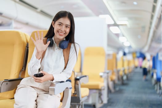 Young asian attractive woman travel by airplane, Passenger wearing headphone putting hand baggage in lockers above seats of plane.