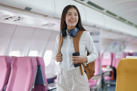 Young asian attractive woman travel by airplane, Passenger wearing headphone putting hand baggage in lockers above seats of plane.