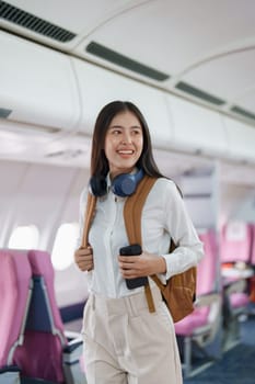 Young asian attractive woman travel by airplane, Passenger wearing headphone putting hand baggage in lockers above seats of plane.