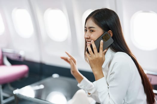 Asian business woman passenger sitting on business class luxury plane while working using smart phone mobile talking or video conference and travel concept.