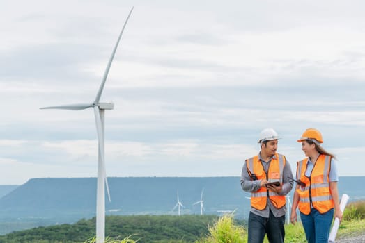 Male and female engineers working on a wind farm atop a hill or mountain in the rural. Progressive ideal for the future production of renewable, sustainable energy.