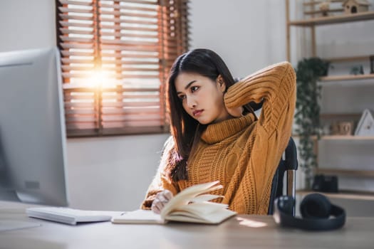 Tired teen asian lady in headphones falls asleep at table with laptop in room interior. Boring video lesson at home, problems at study, education with modern technology, online webinar and overwork..