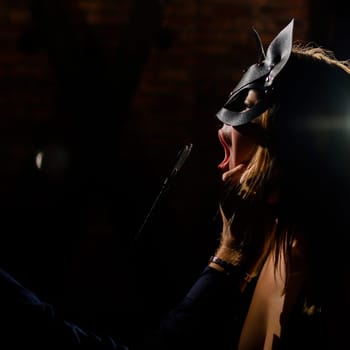 A man in a shirt holds his fingers on the sensual lips of a submissive lover. Portrait Woman in a leather cat mask. BDSM Games for adults