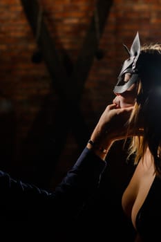 A man in a shirt holds his fingers on the sensual lips of a submissive lover. Portrait Woman in a leather cat mask. BDSM Games for adults.